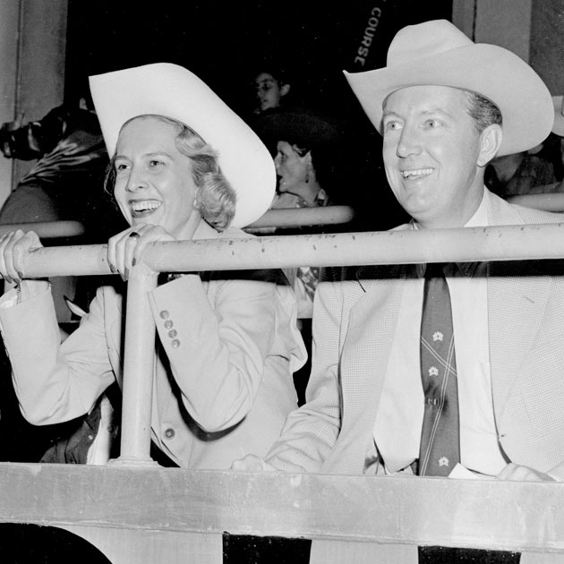 Jane and John Justin smile while cheering at a rodeo.